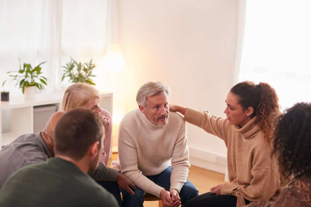 Group therapy session with women comforting a man as a way to help others in recovery.
